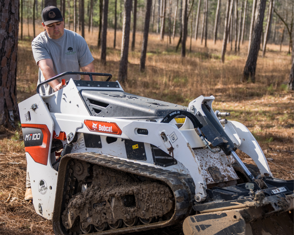 Bobcat track loader in a forest setting with a person operating it.