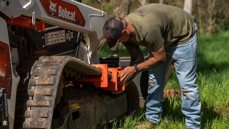 Man in green shirt inspecting orange component on a Bobcat skid steer track