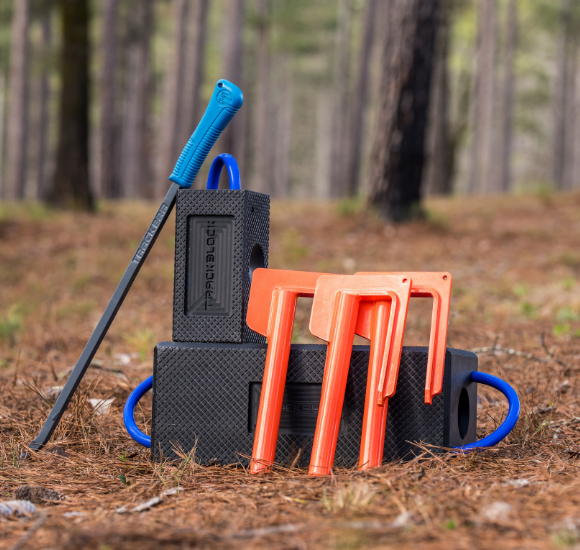 Black track bar system with blue handle tool and orange brackets in a forest setting