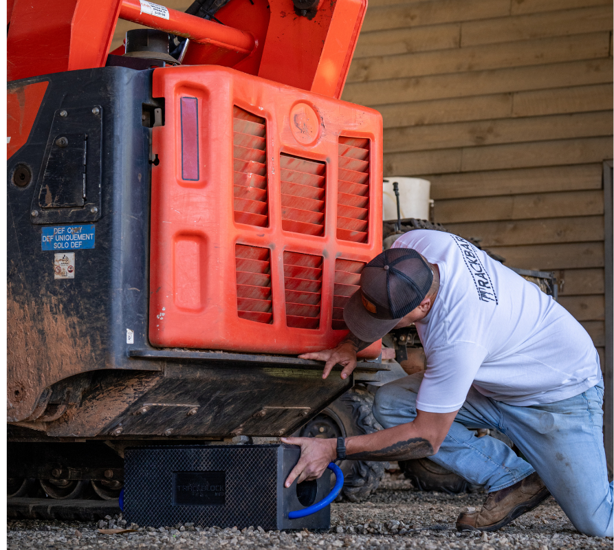Mechanic in white shirt placing a black Trackblock Max under a red compact track loader on gravel