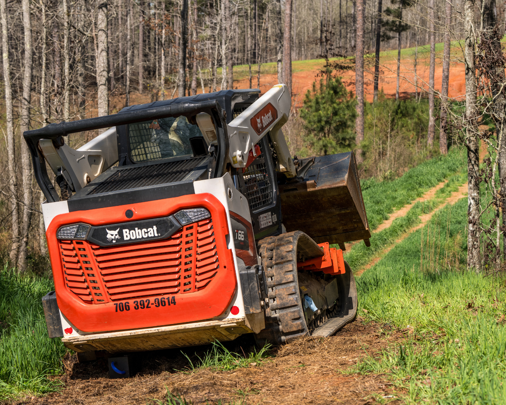 Orange Bobcat T66 compact track loader working on a wooded dirt trail, phone number 706-392-9614 visible
