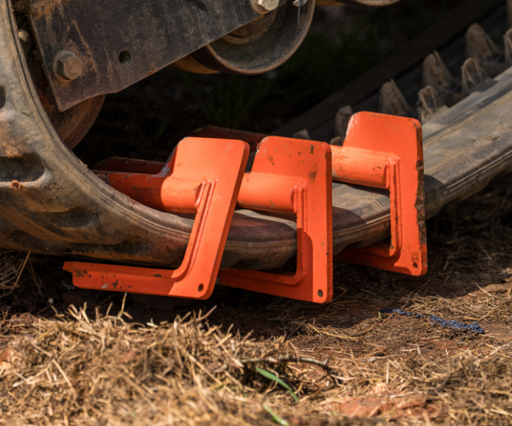 Orange steel track pads clamped onto rubber crawler tracks of heavy equipment on dirt ground
