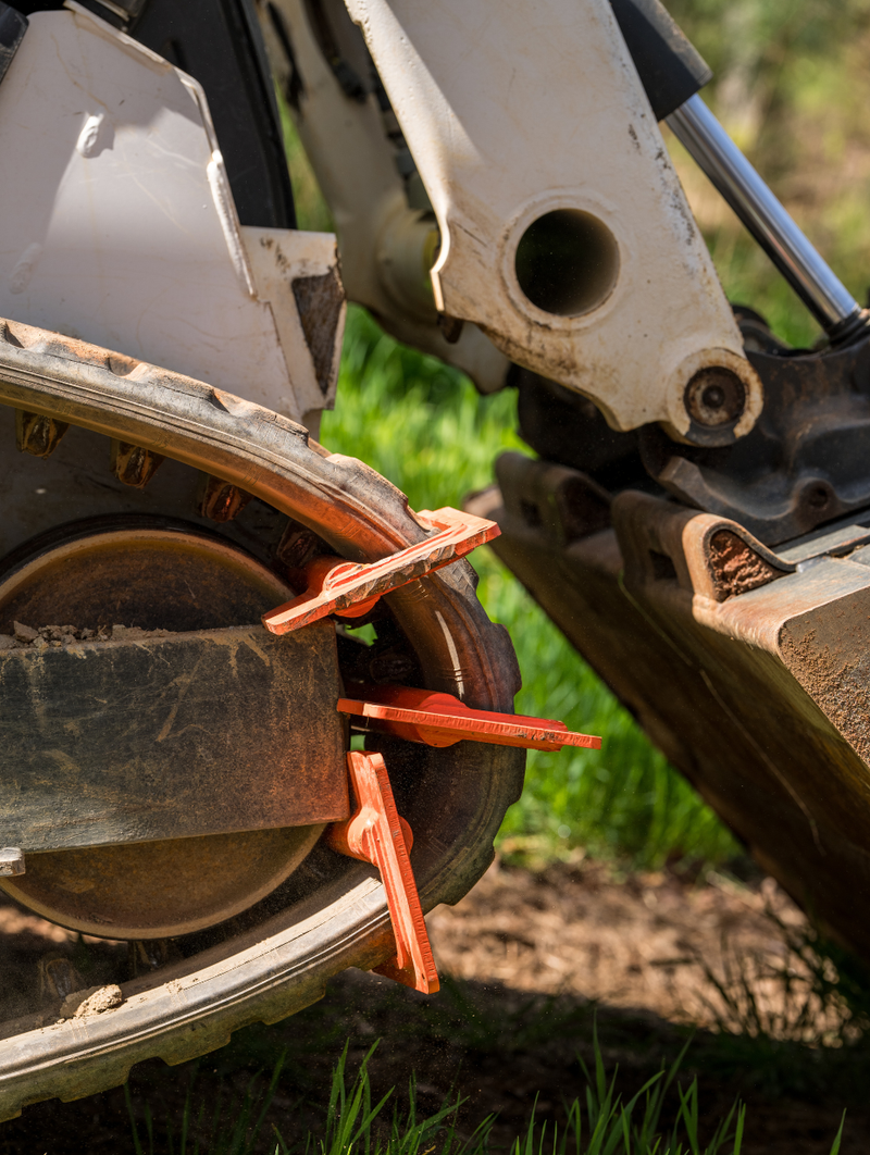 Orange track bar tool clamped onto a muddy dirt bike rear tire and swingarm